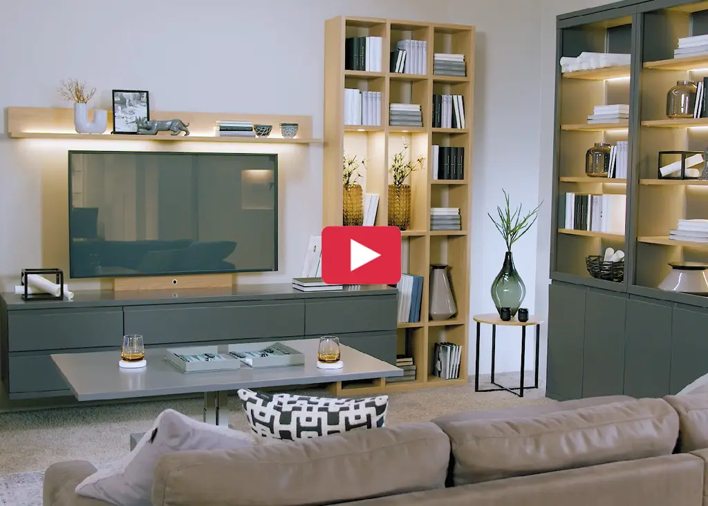 Wohnzimmer mit TV auf Lowboard, Regalwand mit Büchern und Vitrinenschrank rechts, Couchtisch vor Sofa